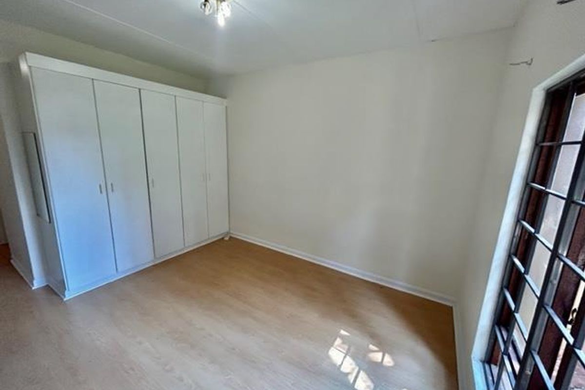 A bright bedroom featuring light wood-look flooring, built-in white cabinetry, and a large window with security bars.