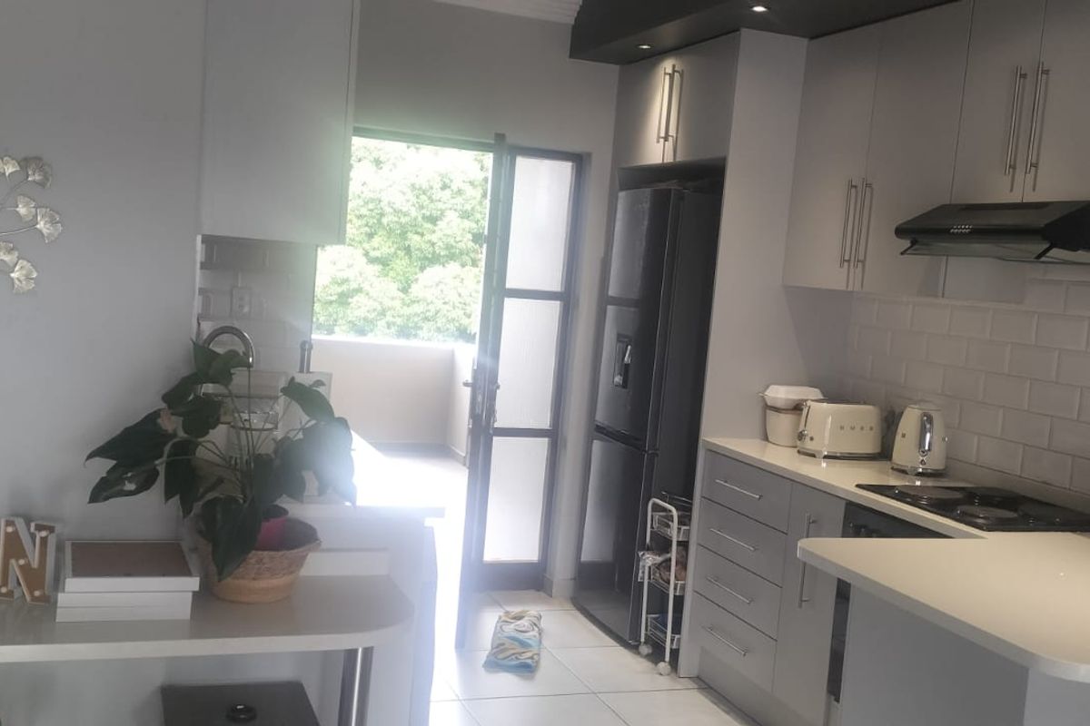 Modern kitchen featuring grey cabinetry, subway tile backsplash, stone countertops, and integrated hob with extractor fan, leading out to a balcony.