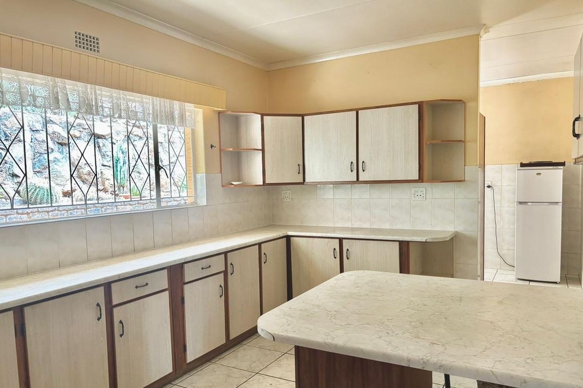 A functional kitchen featuring light-toned cabinetry, laminate countertops, tiled splashbacks, and a breakfast bar, with a window overlooking the exterior garden area.