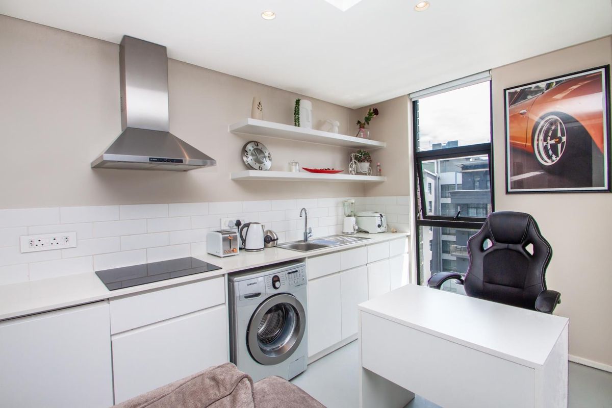 Modern kitchen featuring white cabinetry, subway tile backsplash, stainless steel extractor fan, integrated hob, and built-in washing machine.