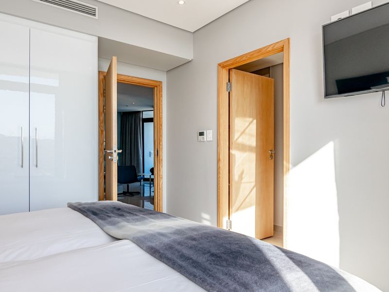 A well-maintained bedroom featuring built-in high-gloss wardrobes, recessed ceiling lighting, and ducted air conditioning with access to an adjoining room.