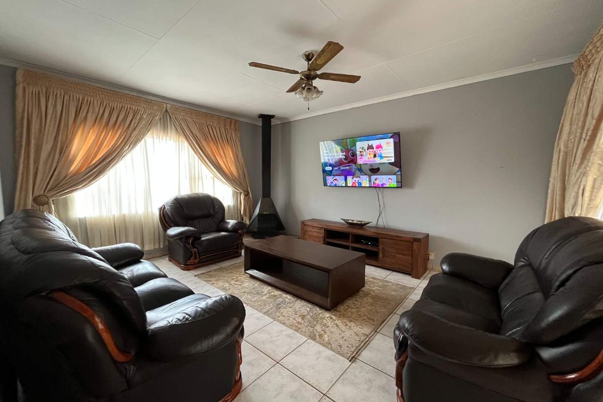 A comfortable living room featuring tiled flooring, a central ceiling fan, and a freestanding fireplace, providing a functional and inviting space.