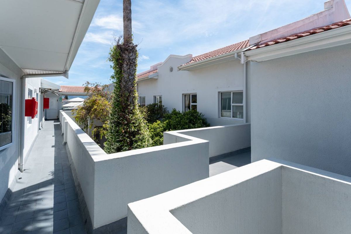 An exterior view of an apartment complex featuring a tiled roof, white parapet walls, and a paved walkway overlooking a central courtyard area.