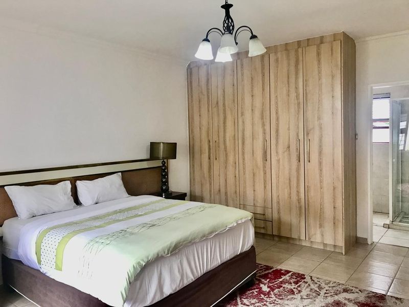 A well-maintained bedroom featuring light wood-grain built-in cupboards, tiled flooring, and an en-suite bathroom access.