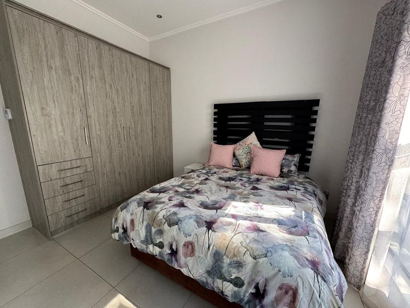 A well-maintained bedroom featuring modern built-in cupboards, neutral tiled flooring, and recessed ceiling lighting, offering a clean and functional living space.