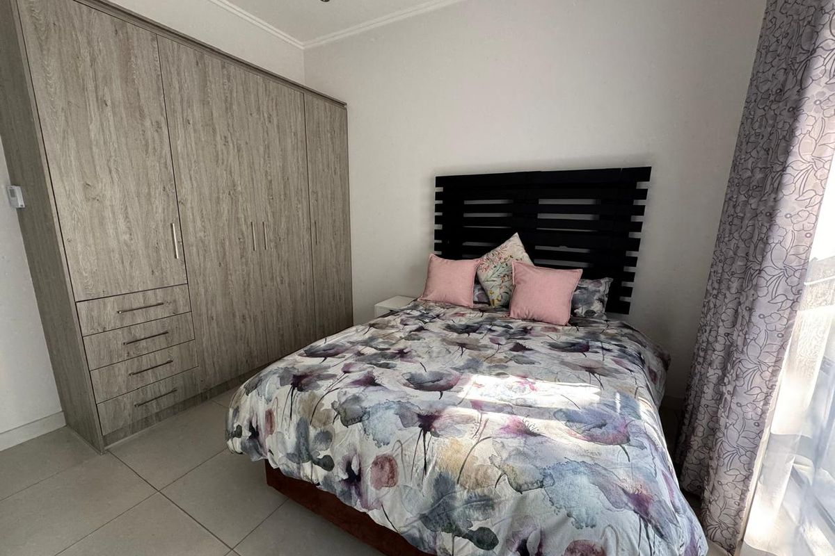 A well-maintained bedroom featuring modern built-in cupboards, neutral tiled flooring, and recessed ceiling lighting, offering a clean and functional living space.