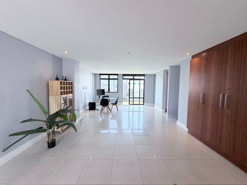 Spacious open-plan living area featuring polished porcelain floor tiles, recessed lighting, and a large built-in wooden wardrobe with ample storage space.