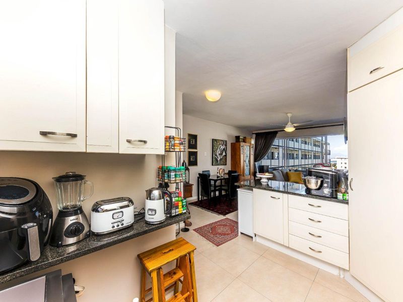 Open-plan kitchen and living area featuring white cabinetry, granite countertops, and tiled flooring, creating a functional and connected living space.