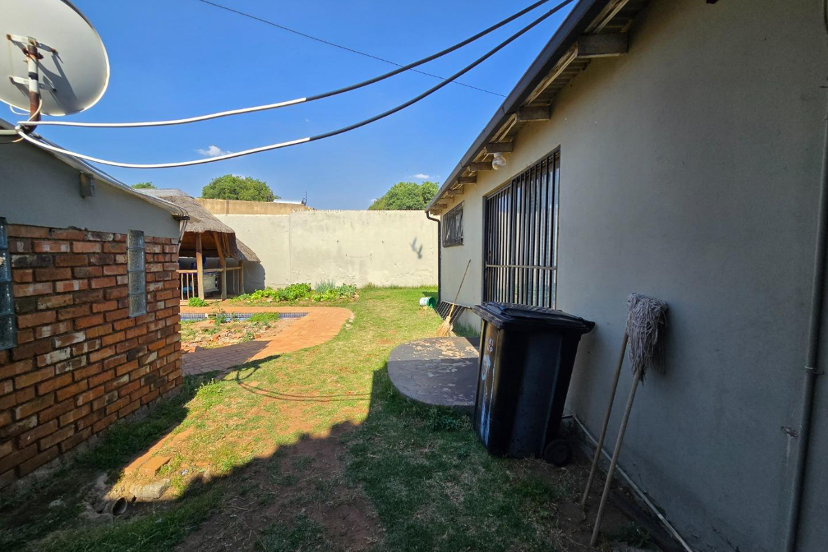 Rear exterior view of the property featuring a brick wall, security bars on windows, and a small concrete patio area in the backyard.