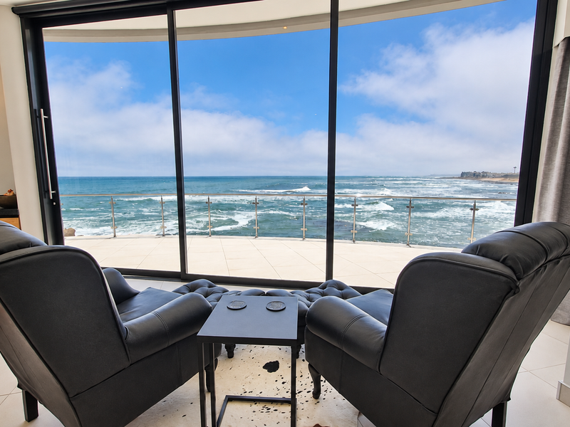 Modern living area featuring expansive floor-to-ceiling sliding glass doors that open onto a balcony with panoramic ocean views.