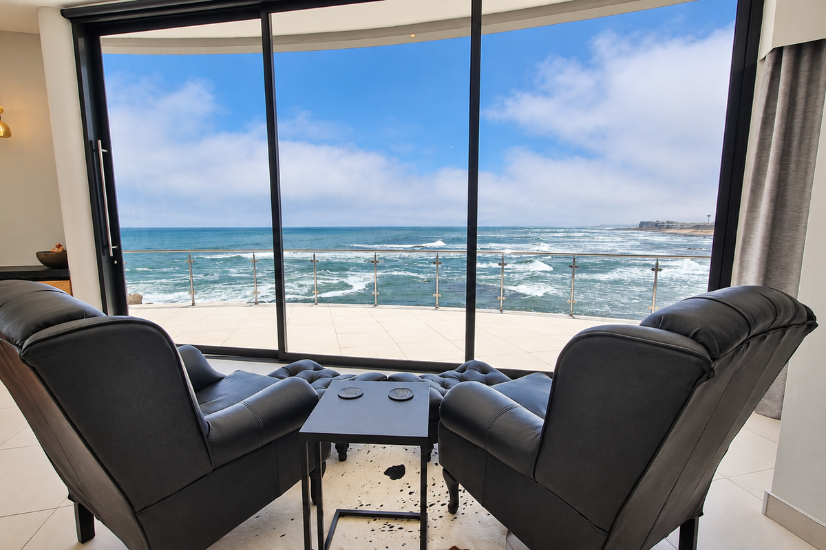 Modern living area featuring expansive floor-to-ceiling sliding glass doors that open onto a balcony with panoramic ocean views.