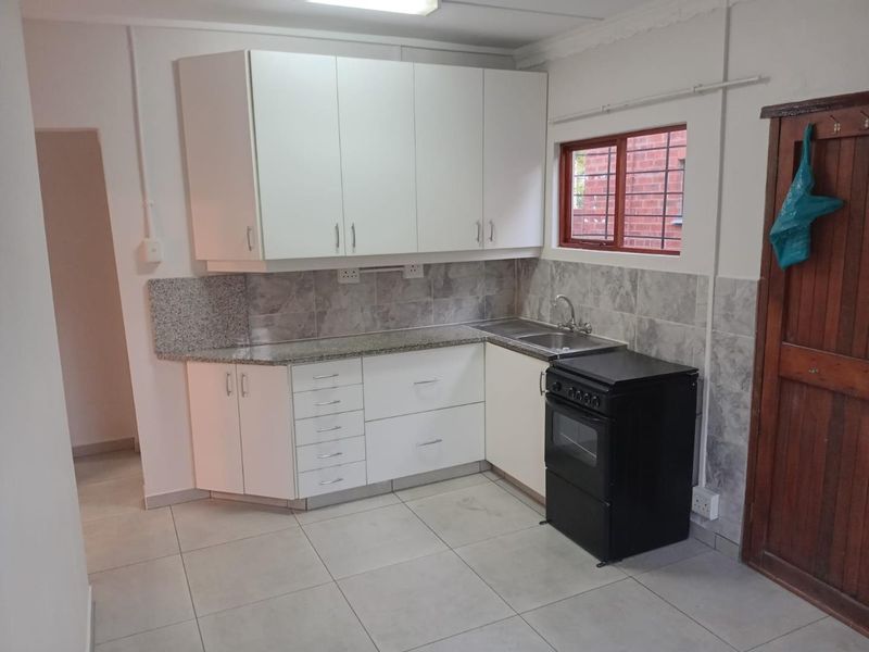 A functional kitchen featuring white cabinetry, granite countertops, tiled backsplash, and ceramic floor tiles, equipped with a freestanding stove and a window with security bars.