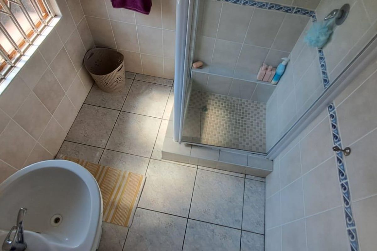 A functional bathroom featuring a tiled shower enclosure, pedestal basin, and security bars on the window.