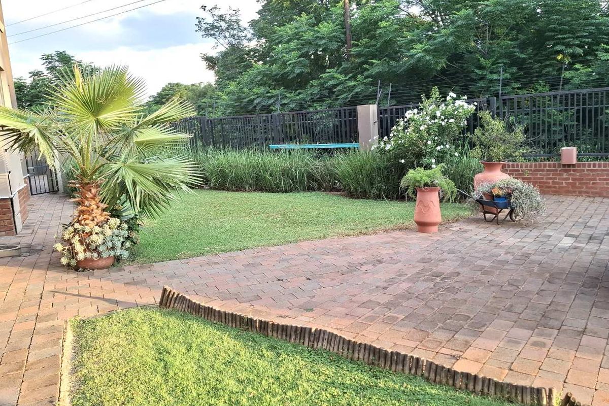 A well-maintained rear garden featuring a paved patio area, manicured lawn, and secure perimeter fencing with established greenery.