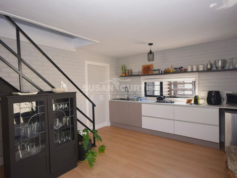Modern kitchen featuring sleek cabinetry, integrated hob, open shelving, and a staircase, set within an open-plan living space with light wood-look flooring.
