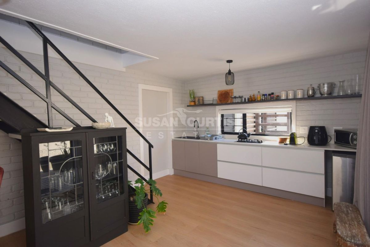 Modern kitchen featuring sleek cabinetry, integrated hob, open shelving, and a staircase, set within an open-plan living space with light wood-look flooring.