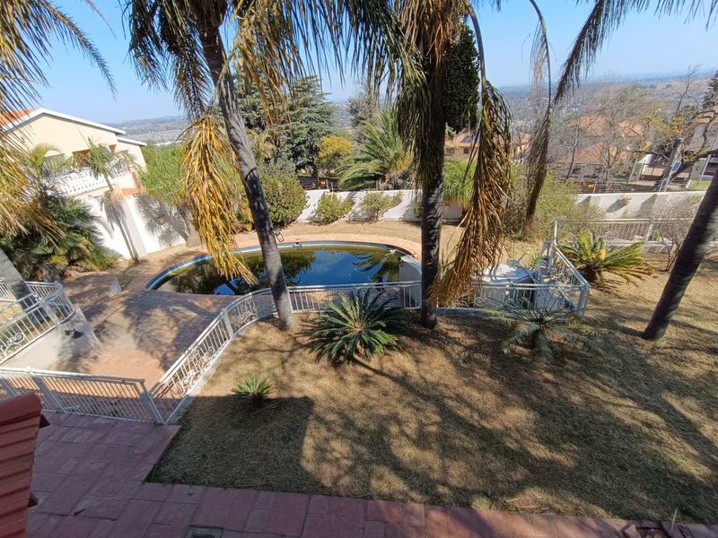 An elevated view of a backyard featuring a swimming pool, paved patio area, and metal safety railings, set within a landscaped garden.