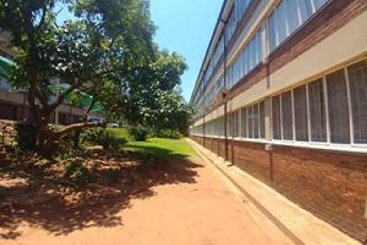 A view of the apartment building's rear exterior, featuring a brick facade, large windows, and an adjacent garden area.