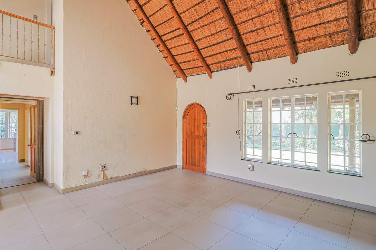 Spacious living area featuring a high vaulted thatched ceiling, tiled flooring, arched wooden door, and large windows allowing for natural light.