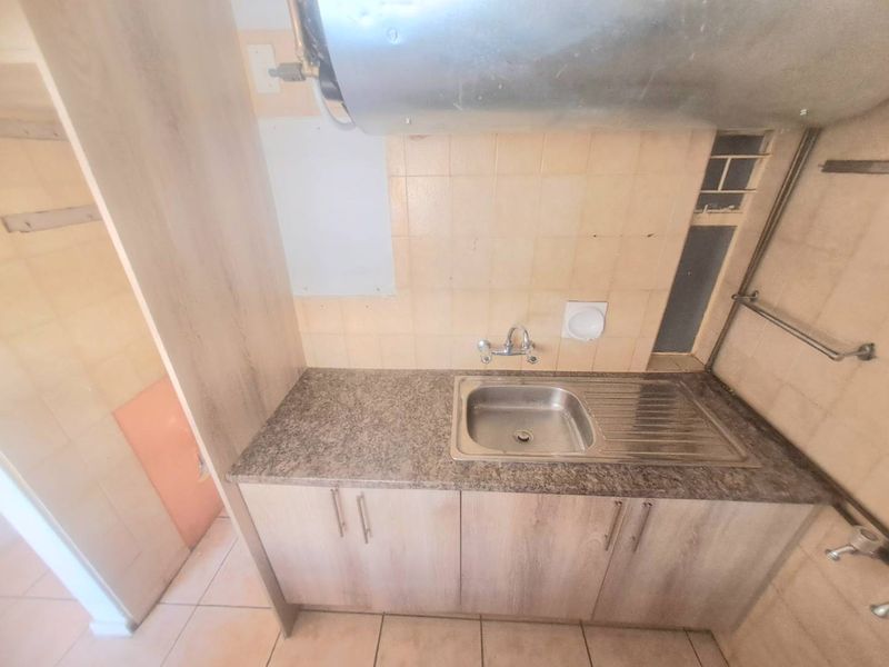 A compact kitchen area featuring a stainless steel sink, laminate countertop, built-in cabinetry, and tiled backsplash, requiring some cosmetic updates.