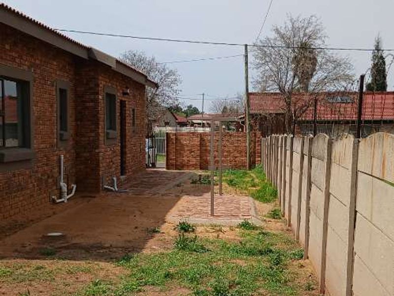 Rear exterior view of the property featuring face brick walls, a paved walkway, and a large unmaintained garden area enclosed by a precast boundary wall.