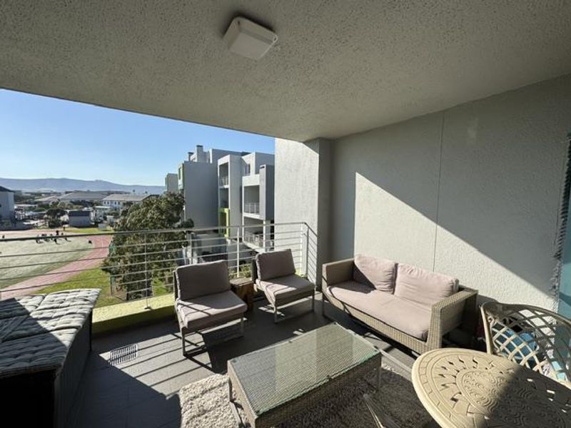 A spacious covered balcony featuring tiled flooring, a stainless steel balustrade, and pleasant views of the surrounding neighborhood.