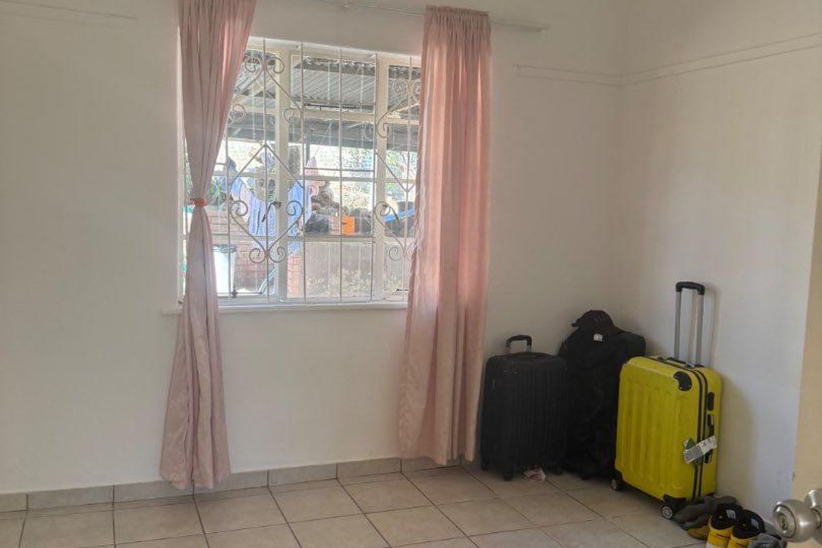 A simple, vacant bedroom featuring neutral tiled flooring, a window with security bars, and a curtain rod, offering a clean canvas for personalization.