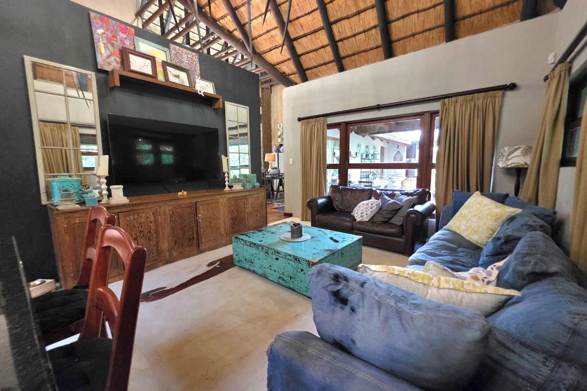 Spacious living room featuring a high vaulted thatched ceiling, exposed timber beams, and large windows providing natural light and garden views.