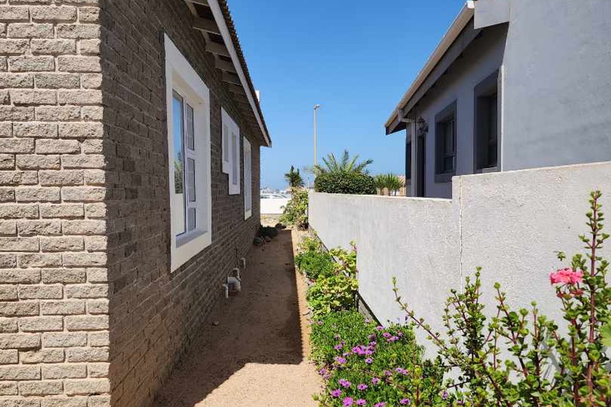 A side exterior walkway between two residential structures, featuring brick and rendered wall finishes with a gravel path and landscaped garden border.