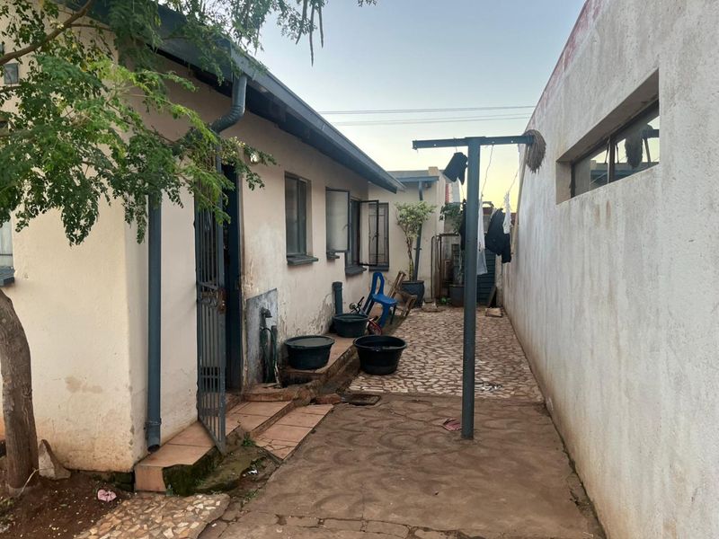 A narrow side exterior area featuring paved ground, a metal washing line, and access to the side of the house with visible exterior wall wear.