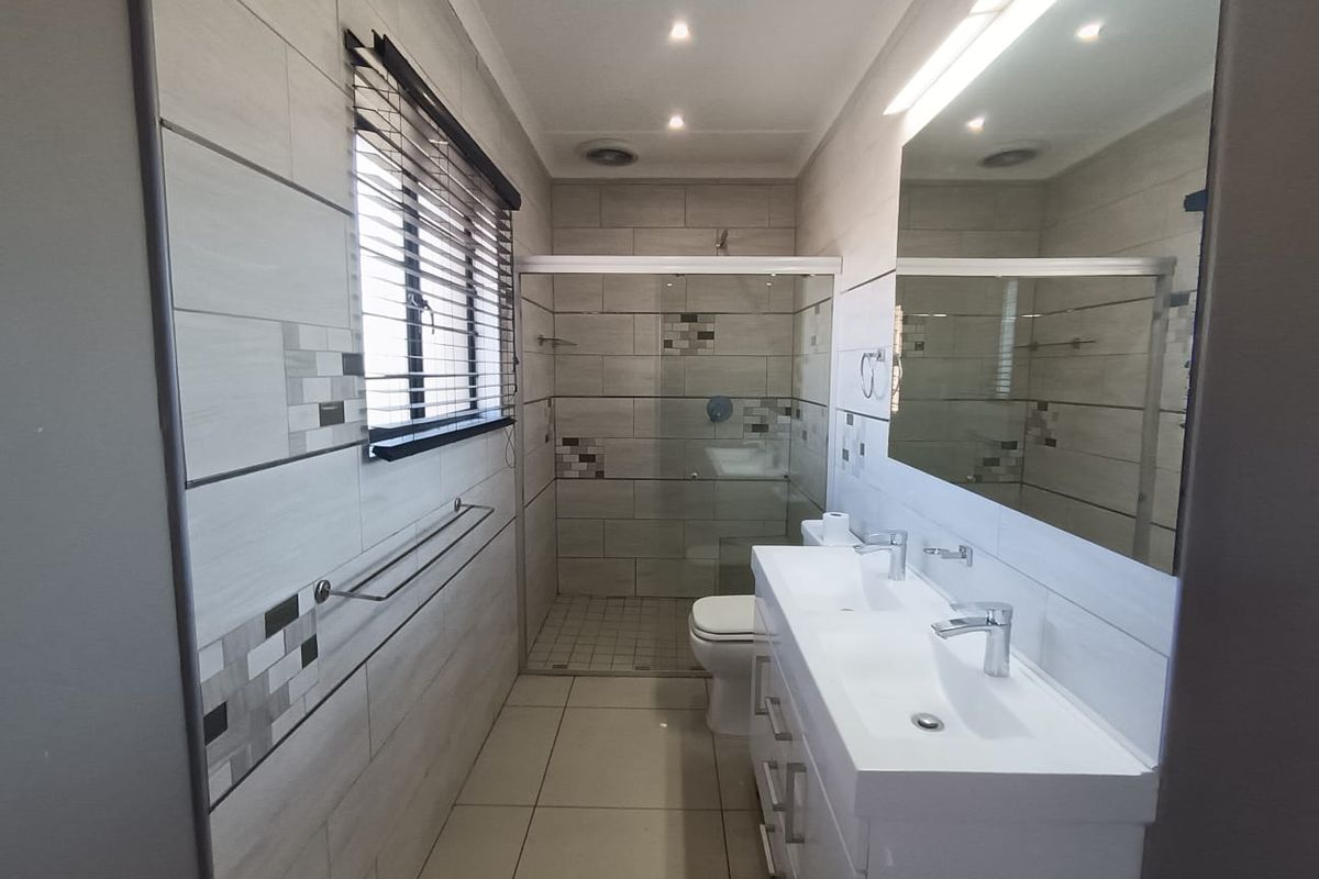 Modern bathroom featuring a double vanity, large wall mirror, and a spacious glass-enclosed shower with neutral tiled finishes.