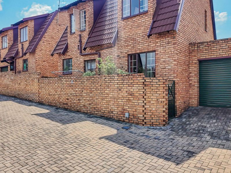 Front exterior view of a face brick townhouse complex featuring a paved driveway, secure garage access, and a private boundary wall.