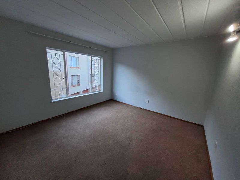 An empty bedroom featuring carpet flooring, ceiling panels, and a large window with security bars, offering a blank canvas for renovation.