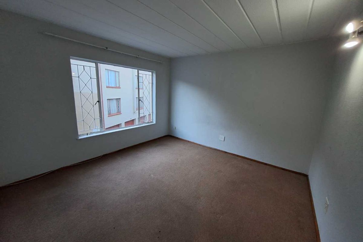 An empty bedroom featuring carpet flooring, ceiling panels, and a large window with security bars, offering a blank canvas for renovation.