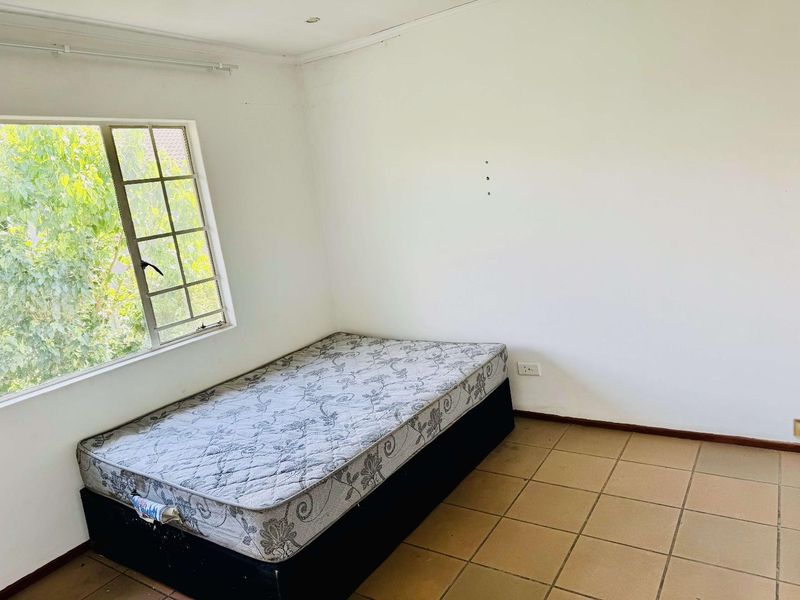 A simple bedroom featuring tiled flooring and a window with security bars, offering a blank canvas for potential interior design updates.