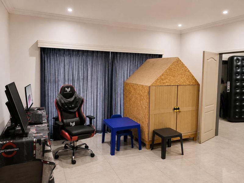A bedroom featuring tiled flooring, recessed downlights, and a large window with curtain tracks, currently utilized as a multi-purpose play and office space.