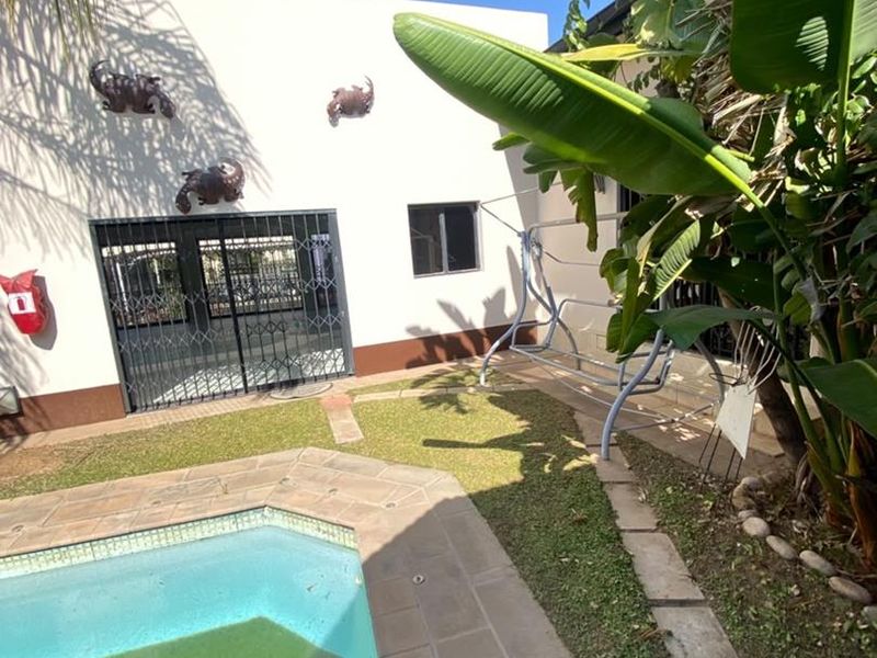 Outdoor pool area featuring a paved surround, security gate, and wall-mounted fire extinguisher, set within a landscaped garden space.