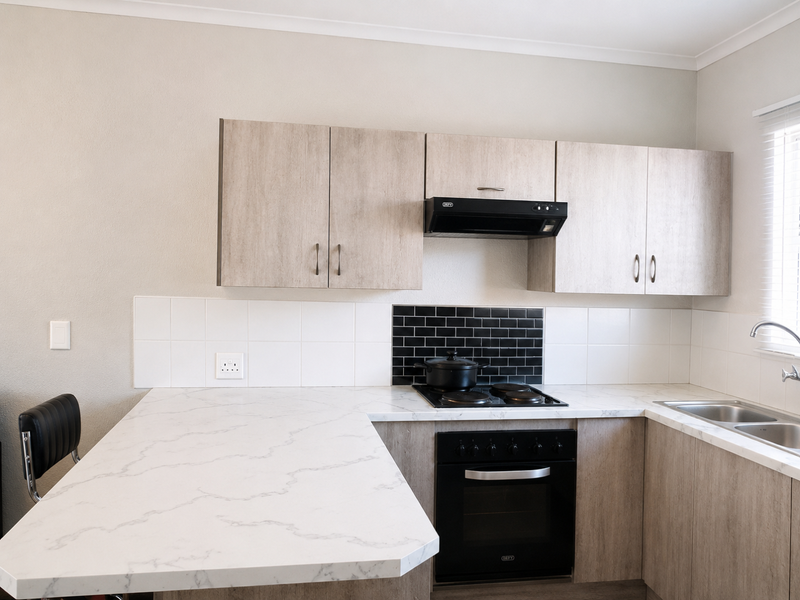 Modern kitchen featuring light wood-grain cabinetry, marble-effect countertops, a black tiled backsplash, and integrated appliances including an oven and extractor fan.