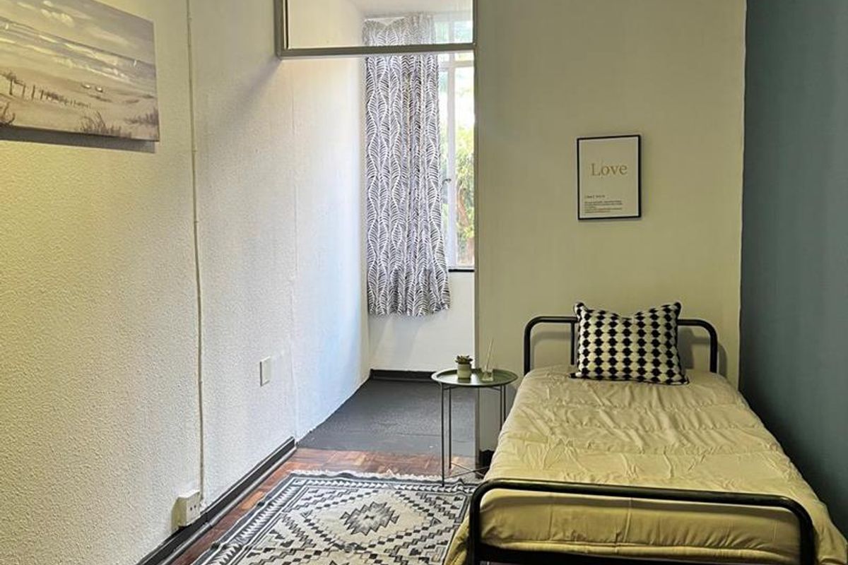 A compact bedroom featuring original parquet flooring, a feature wall, and a large window providing natural light.