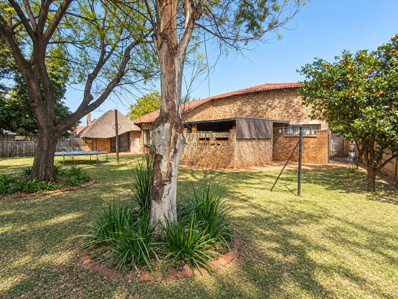 Spacious rear garden featuring a brick-built exterior, a traditional thatched lapa, and established trees, offering a private outdoor living space.