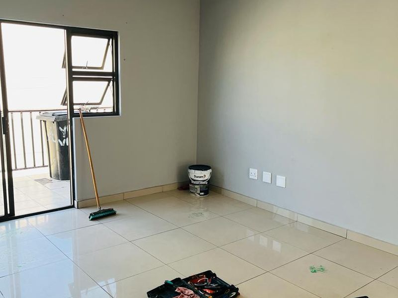 An empty, well-lit living area featuring neutral grey walls, polished floor tiles, and a sliding door providing access to an outdoor balcony.