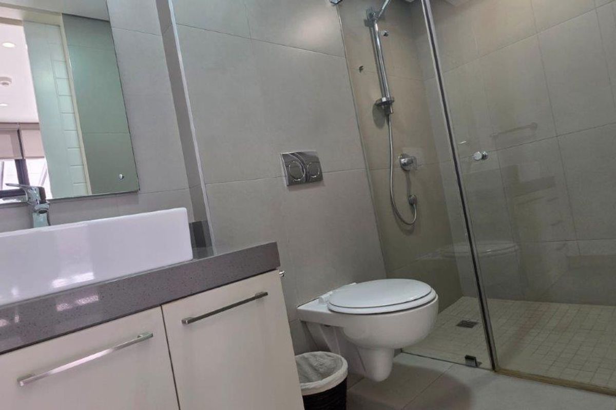 Modern bathroom featuring a wall-mounted toilet, glass-enclosed shower, and a sleek vanity with a countertop basin.