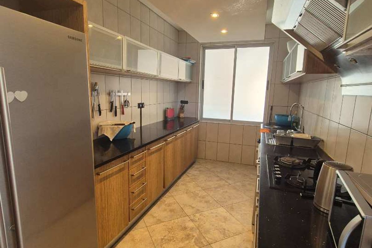 A functional galley-style kitchen featuring wood-finish cabinetry, black granite countertops, tiled flooring, and a built-in gas hob with an extractor fan.