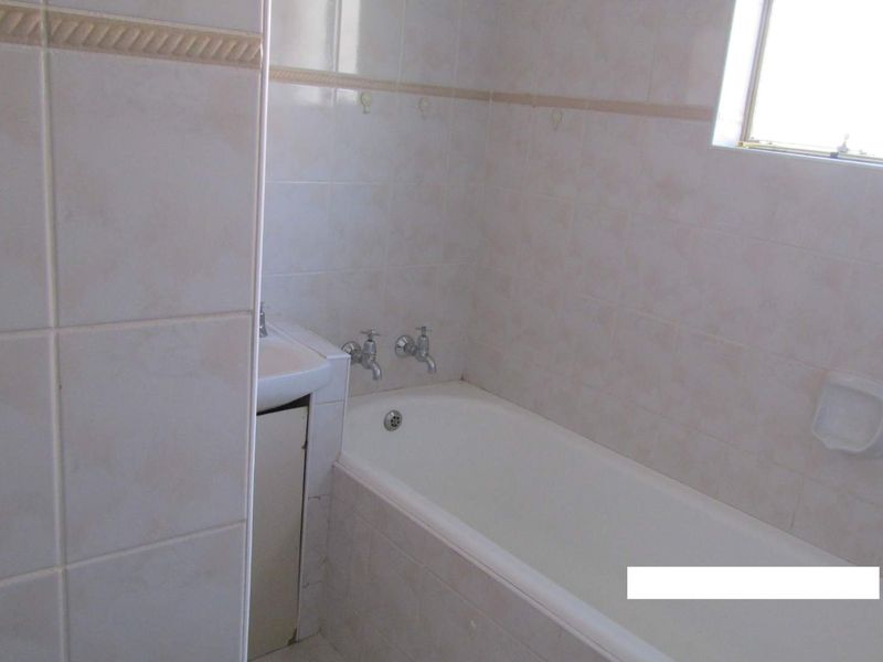A functional bathroom featuring a standard bathtub, pedestal basin, and neutral wall tiling.