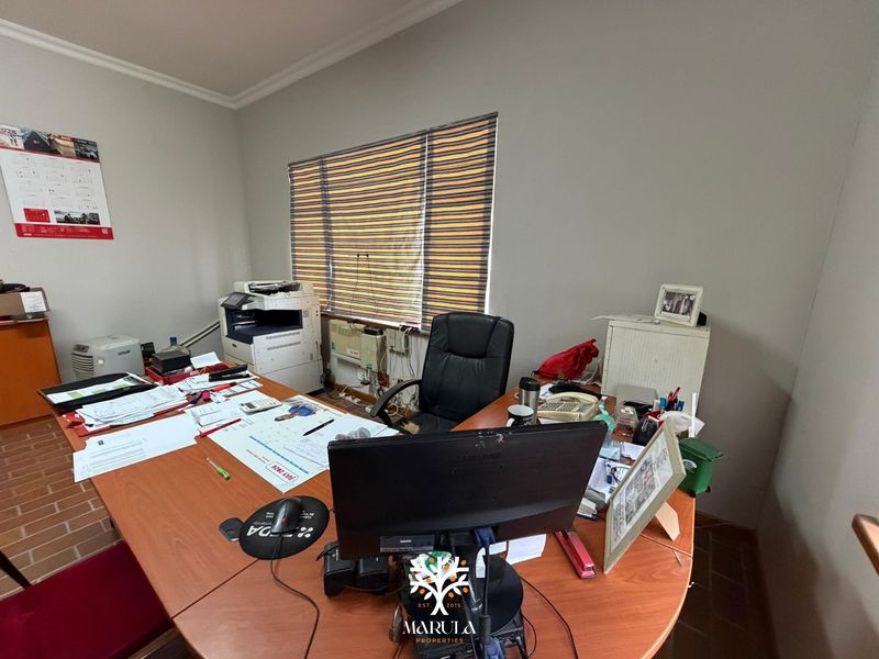 A functional office space featuring a window with blinds and a wall-mounted air conditioning unit.