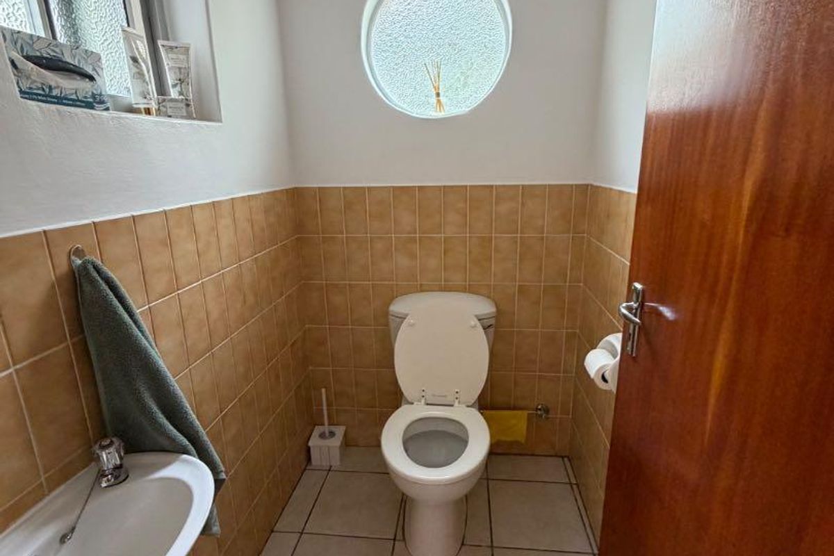 A compact guest bathroom featuring a wall-mounted basin, a standard toilet, and distinctive circular window with neutral tiled finishes.