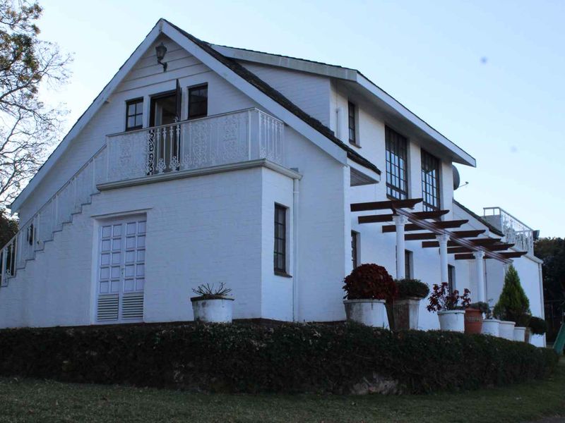 Rear view of a white painted brick residence featuring a balcony with wrought iron railings, a timber pergola, and an external staircase.