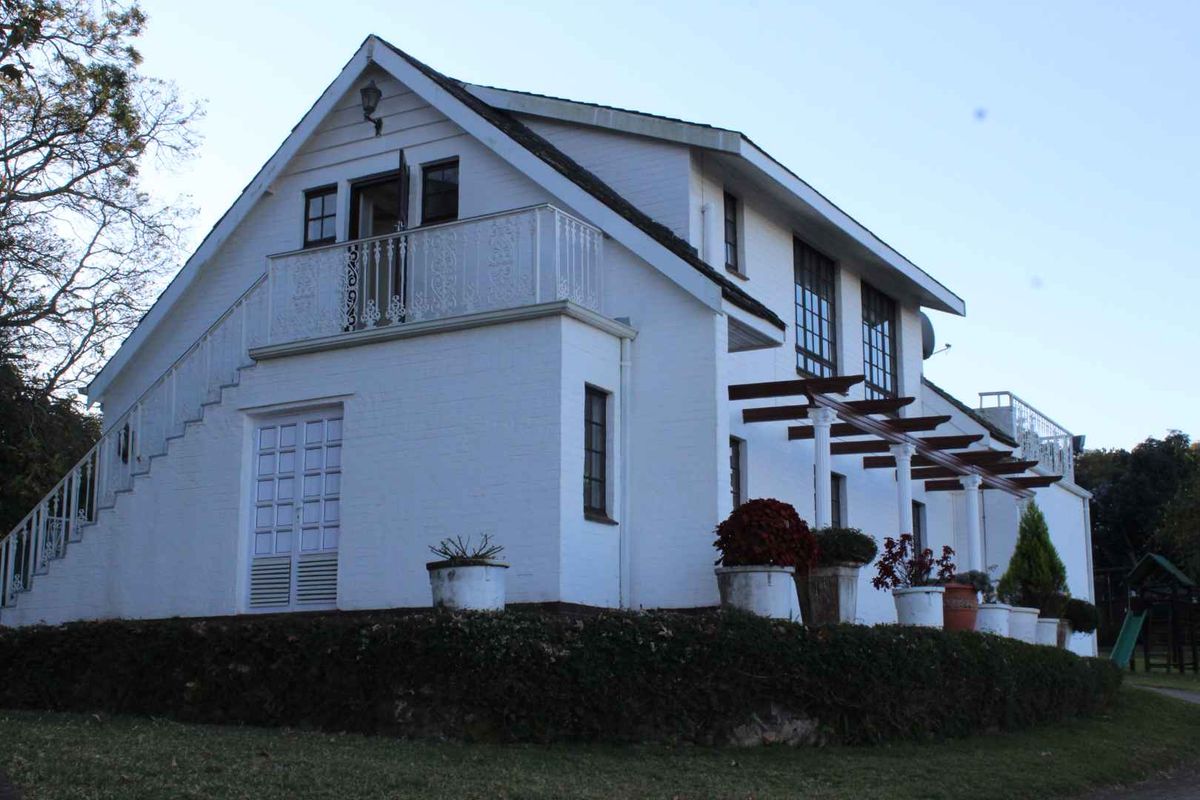 Rear view of a white painted brick residence featuring a balcony with wrought iron railings, a timber pergola, and an external staircase.
