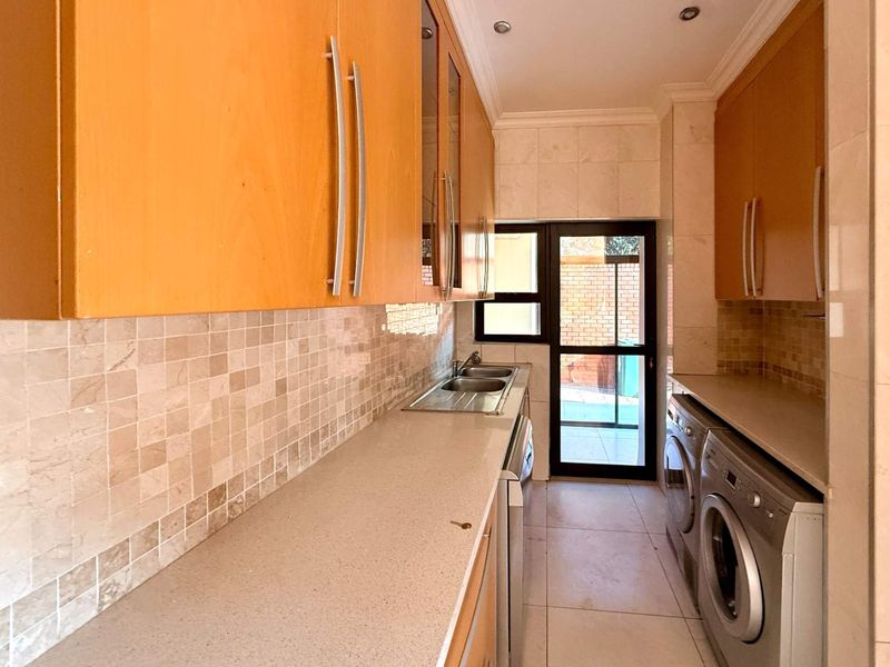 A functional scullery featuring light wood cabinetry, stone countertops, a double sink, and tiled finishes with direct access to the exterior.