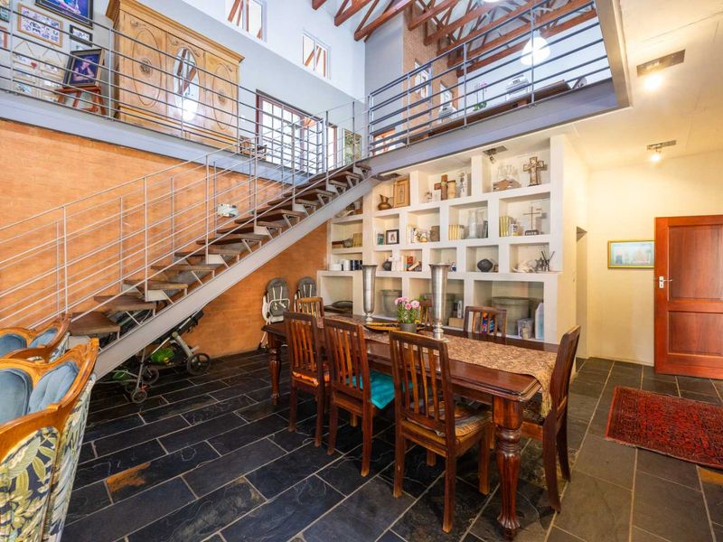 Spacious living area featuring double-volume ceilings with exposed timber trusses, a mezzanine level, slate flooring, and a large built-in feature shelving unit.